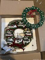 Two wreaths in box - one large sculpted with mini village houses and one smaller green wreath