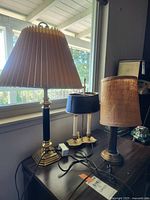 Photo of three table lamps on a wooden surface near window, showing different styles and shades.