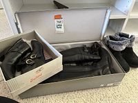 Three pairs of ladies' winter boots including two pairs of black leather tall boots and one pair of black ankle boots with faux fur lining, shown in their boxes on carpet floor.