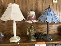 Wide front view showing all three lamps side by side on shelf against wooden panel background.