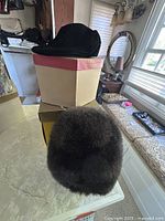 Four vintage hats and two vintage hat boxes displayed on a marble surface in front of a window and furniture backdrop.