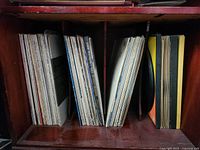 Vinyl records standing vertically in three rows on a wooden shelf showing edges of album covers.
