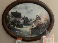 Framed oval print depicting Alderton Village by Marty Bell, showing the entire artwork in the wooden frame.