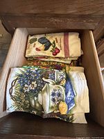 Drawer containing folded dish towels with floral and kitchen motif prints, featuring soft earth tones and colorful floral designs.