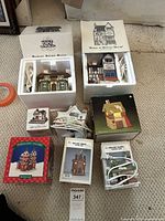 Photo showing seven assorted Christmas village houses, some boxed, with electric light cords visible.