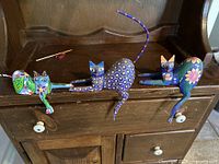 Three colorful and intricately painted cat figurines with long tails and detailed patterns sitting on a cabinet shelf.