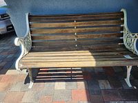 Front view of the wooden slat bench with white cast iron ornamental sides, showing weathered wood condition.