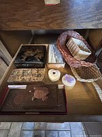 Drawer containing assorted decorative and carved wooden boxes, heart-shaped boxes, and several woven baskets of different shapes and colors including a gold color basket with handle.