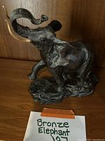 Front angle of the bronze elephant sculpture on a wooden surface with a handwritten label 'Bronze Elephant'.