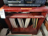 Front view of reddish-brown wooden cabinet with upper shelf and lower divided compartment containing vinyl records, showing scratches and wear.