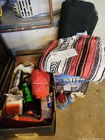 Photo showing box filled with assorted camping gear including thermos, green WWF water bottle, rolled blanket, red bag, lanterns, and portable TV box