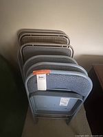 View of four blue-gray padded folding chairs from the back arranged in a row, showing metal frame construction and padded seats and backs.