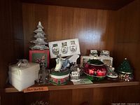 Shelf with various Christmas decorations including Thomas Kinkaid ornaments, glass figurines, and decorative tins.