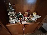 Wide view of all Christmas decorations including the Thomas Kinkade Wonderland Express light up tree and assorted figurines on wood cabinet.