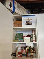 Photo showing assorted Christmas decorations inside shelving including boxes, a Grand Carousel music box, glass ornaments, and wrapped decorations.