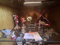 Shelf with two Coca-Cola vintage figurines dressed in red and colorful mosaic skirts, along with other small collectibles such as a miniature violin, gramophone, animal figures, and other decorative items.