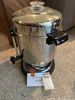 Coffee maker metal body with black handle and dispenser lever on side.