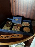 Photo showing a box with multiple commemorative coins, some round, in plastic cases and a Captain James Cook gold plated coin in blue card.
