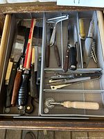 Overview of multiple knives, peelers, and kitchen tools in a metal utensil tray