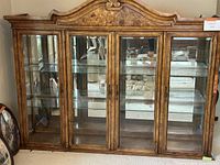 Front view of the full dining hutch top showing four glass doors, glass shelving, wooden frame with detailed carved top molding, and mirrored back inside.