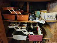 Four fishing tackle boxes on a wooden shelf. Orange, white, and red in color. Includes various fishing gear items inside.