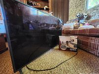 Side view of LG 49-inch flat screen TV leaning against carpeted floor with full-motion wall mount box nearby.