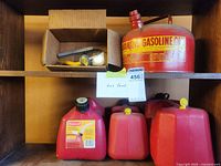 Shelf containing four red gas cans and a small cardboard box with funnel and nozzles.