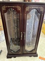 Closed wooden jewelry cabinet with etched glass doors and brass handles