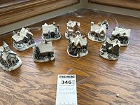 Top-down photo showing all 10 small snow-covered village ornaments including a church and cottages arranged on a wooden surface.