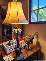 Tall lamp with beige lampshade and monkey and palm tree base seen in room with window and other items.