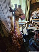 Photo of large giraffe figurine in indoor room setting next to a chair and curtain.
