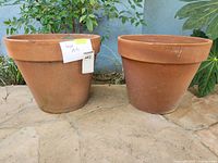Photo of two large terracotta pots side by side on stone patio floor, natural reddish-brown color with minor weathering marks.