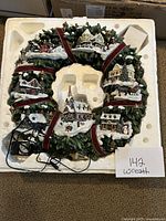 Full view of the wreath in its styrofoam packaging with attached power cord and control switch visible.