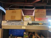 Shelf view showing multiple Lionel boxes: Illuminated Freight Station, Pair of Remote Switches, Chesapeake Flyer long box and unidentified cardboard box