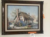 Framed artwork of a thatched cottage with flowers and ducks in a countryside scene.