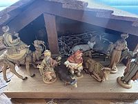 Wide angle of entire manger scene with figurines displayed in front of wooden stable with straw inside.