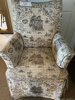 Front view of armchair showing fabric upholstery with detailed antique map and ship pattern, cushioned seat and armrests, and full skirt.