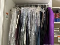 General view of men's dress shirts hanging on a rod, mostly covered in protective plastic sleeves