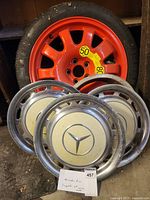 Photo of four wheel rims including three silver Mercedes rims with center caps and one orange spare rim without center cap.