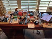 Wide angle photo showing a large assortment of office supplies including binders, staplers, clips, tape, scissors, notepads, and small boxes on a desk.