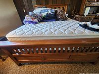 View of queen size bed frame footboard, mattress with quilted cover and pile of linens