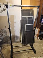 Metal rolling clothing rack in garage setting, with some other items in background.