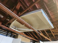 Beige row boat with blue stripe stored in garage rafters.