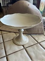 Image of cream-colored Lenox raised shallow pedestal bowl, showing decorative beaded and scalloped edge and pedestal base. Visible repaired crack.