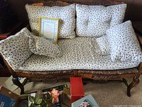 Front view of wood framed settee with floral cushions and a framed poem on the seat.