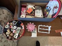 Top view of assorted sewing supplies including boxes, a pink pin cushion, white spool rack, and packs of buttons and thread.