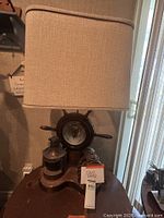 Full view of the large wooden ship themed lamp with beige fabric shade and metal lantern on wooden base.