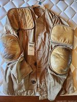 Full view of tan shooting jacket made of army twill with leather padded patches on shoulders and elbows showing wear.