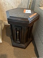 Vintage hexagonal wooden side table cabinet with carved paneling and textured door handle seen from front angled view.