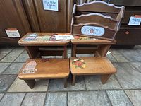 Two wooden stepstools displayed side by side in front of wooden cabinetry. One stepstool has painted houses and the other a floral pattern. The wall-mounted sorting box sits behind them with a floral painted panel.